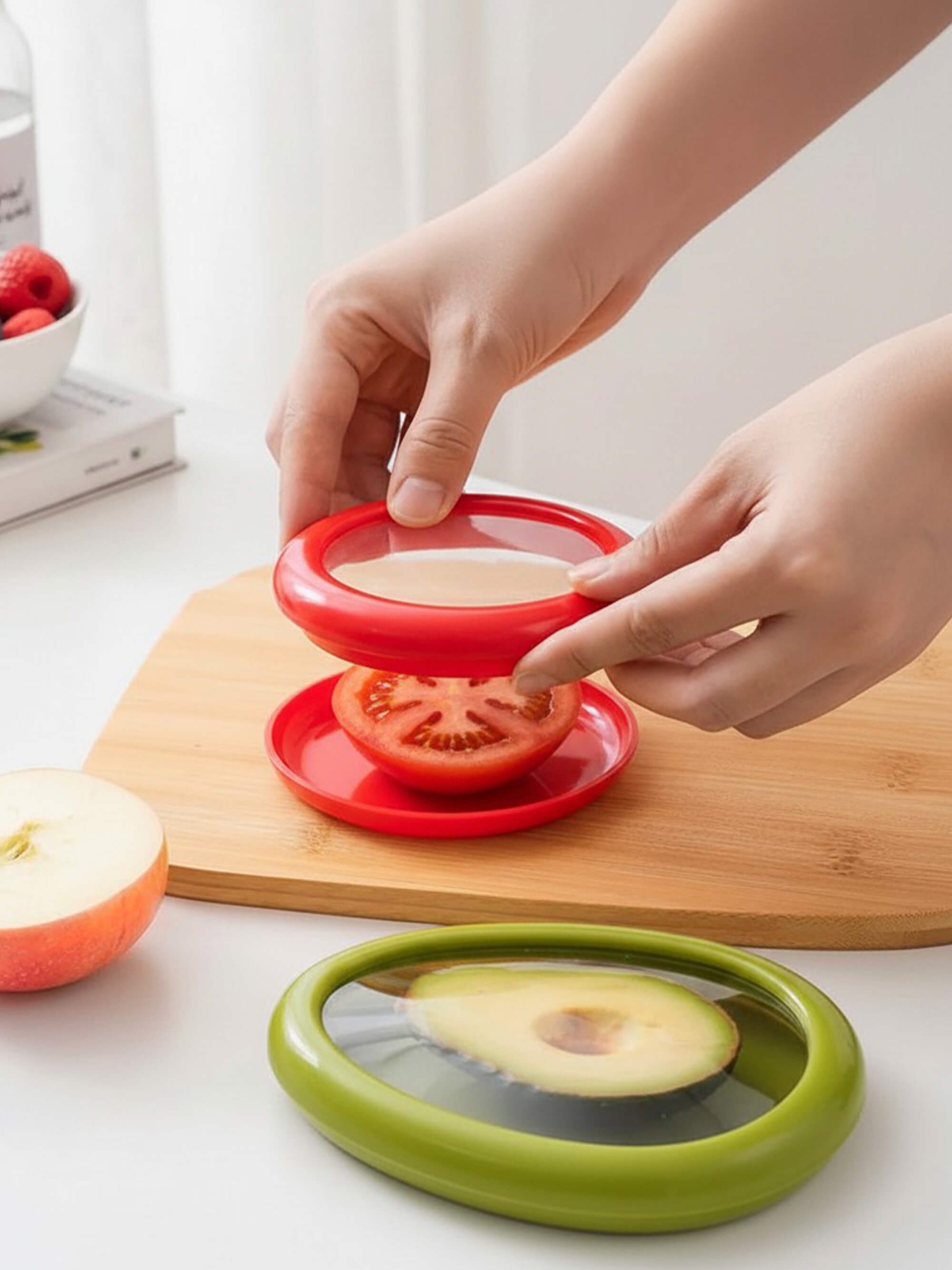 Silicone food saver lid covering half a tomato on a kitchen board for fresh storage